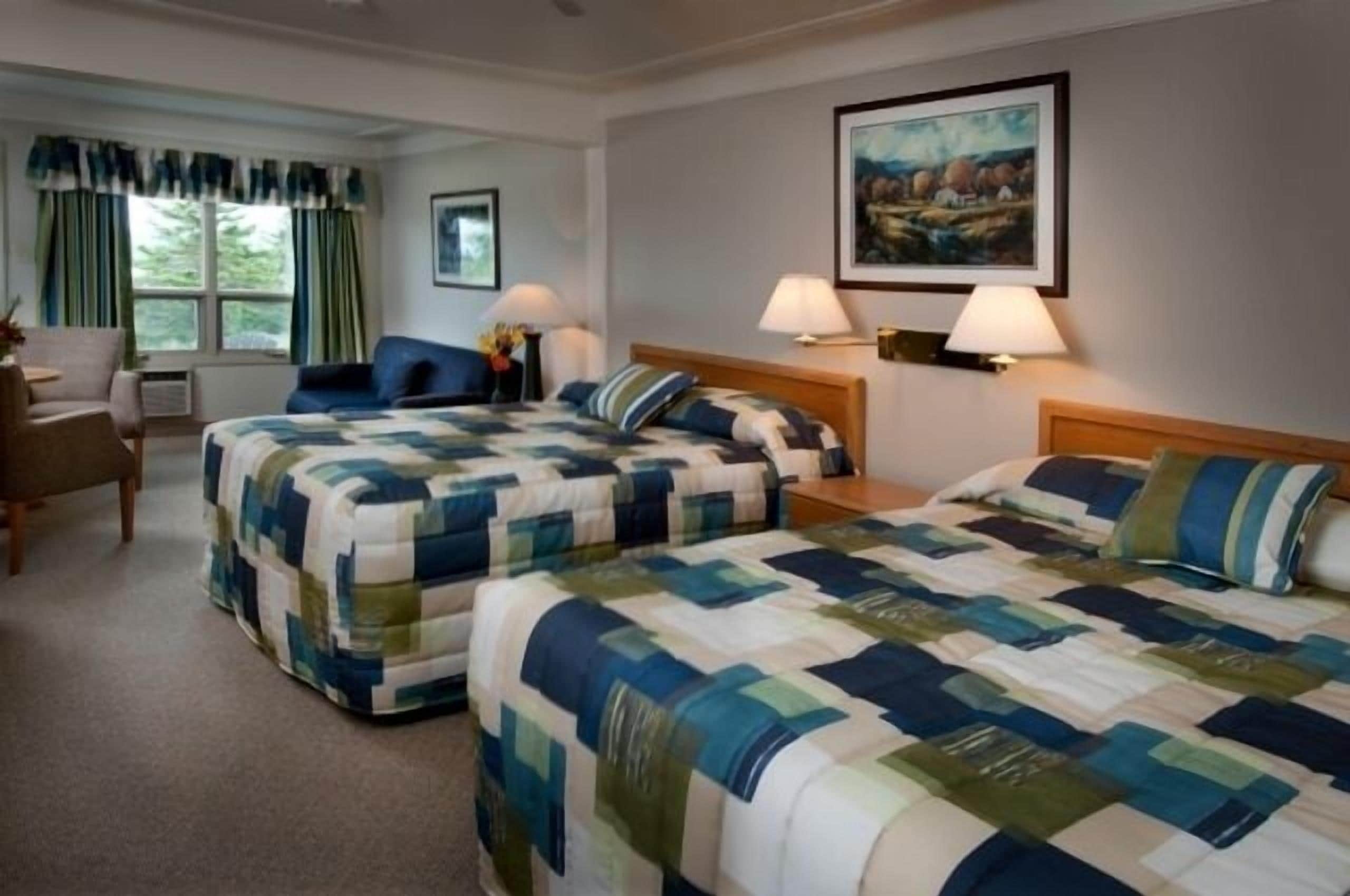 Een hotelkamer met twee bedden, een stoel, een bureau en een schilderij aan de muur.