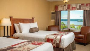 A hotel room with two beds, a chair, a table, and a view of a lake. - Silver Dart Lodge (Baddeck)