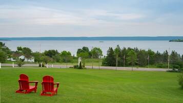 A grassy area with two red Adirondack chairs facing a body of water.