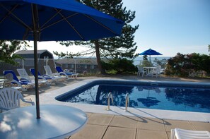 A swimming pool with lounge chairs and umbrellas, surrounded by a fence and trees. - Silver Dart Lodge (Baddeck)