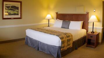 A neatly made bed with a plaid bedspread and a skirted skirt, two bedside lamps, a framed picture on the wall, and a wooden headboard.