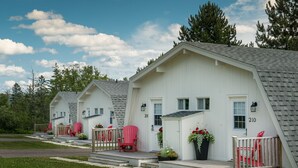 A row of white cabins with numbered doors, red Adirondack chairs on the porch, and potted plants. - Silver Dart Lodge (Baddeck)