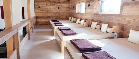 A long room with wooden walls and ceiling, multiple beds with pillows and blankets, and a window on the right wall.