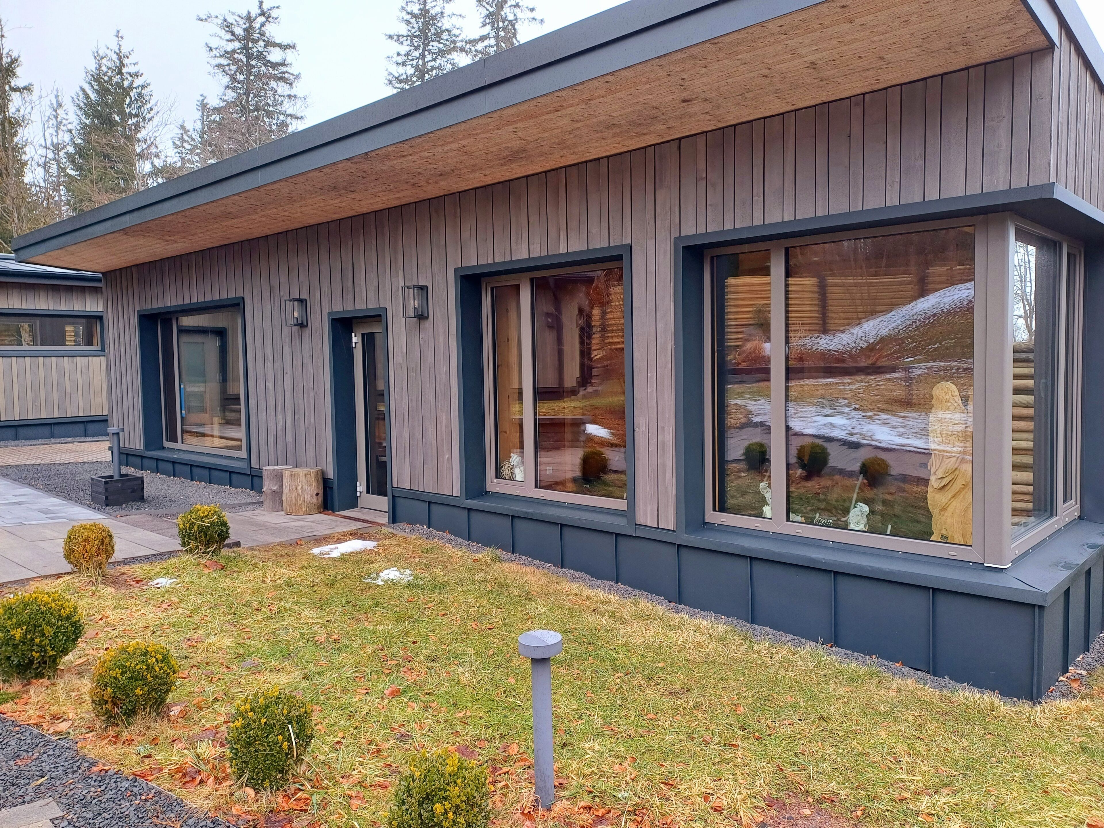 A modern house with large windows, a wooden exterior, and a well-maintained garden.