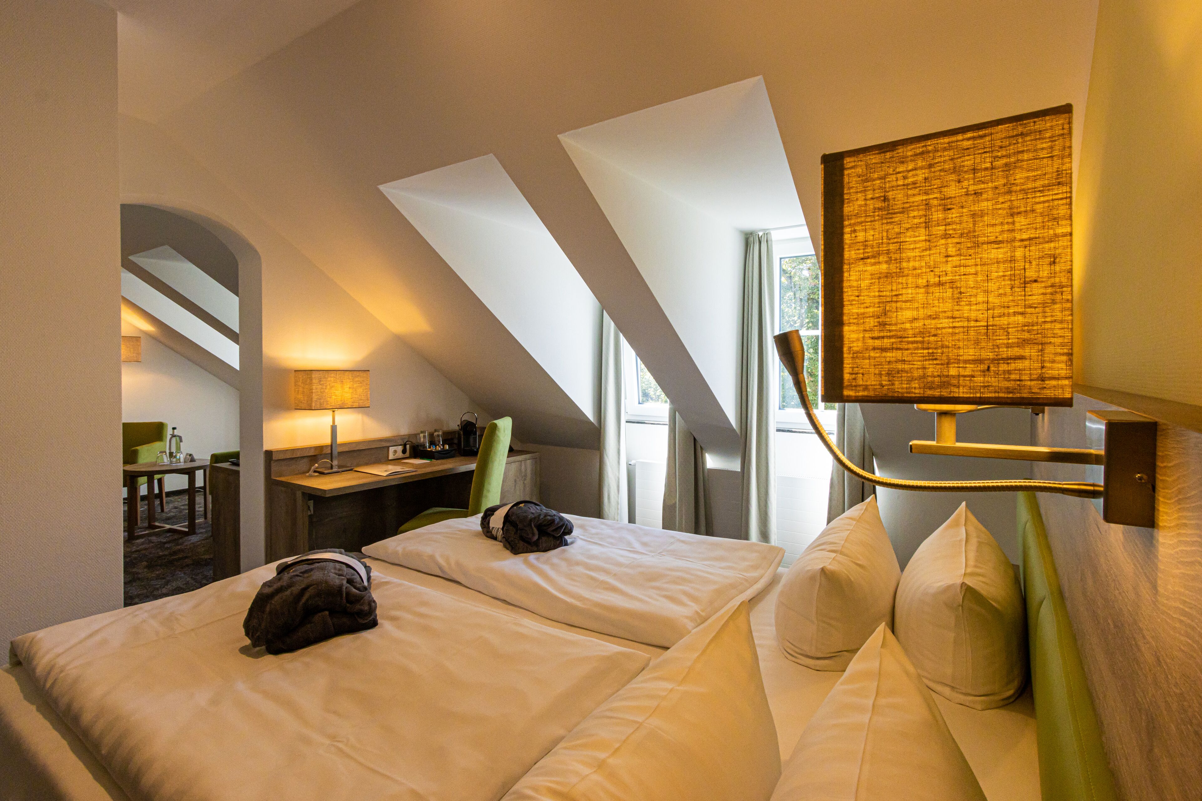 A hotel room with two beds, a desk, a chair, and a large window.