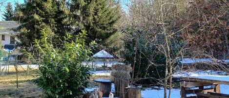 Ambiente rurale all'aperto con una struttura in legno, un grande abete sempreverde e terreno innevato.