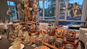 Un bufé con diversas opciones de comida y condimentos, incluyendo frascos con salsas, nueces y frutas.