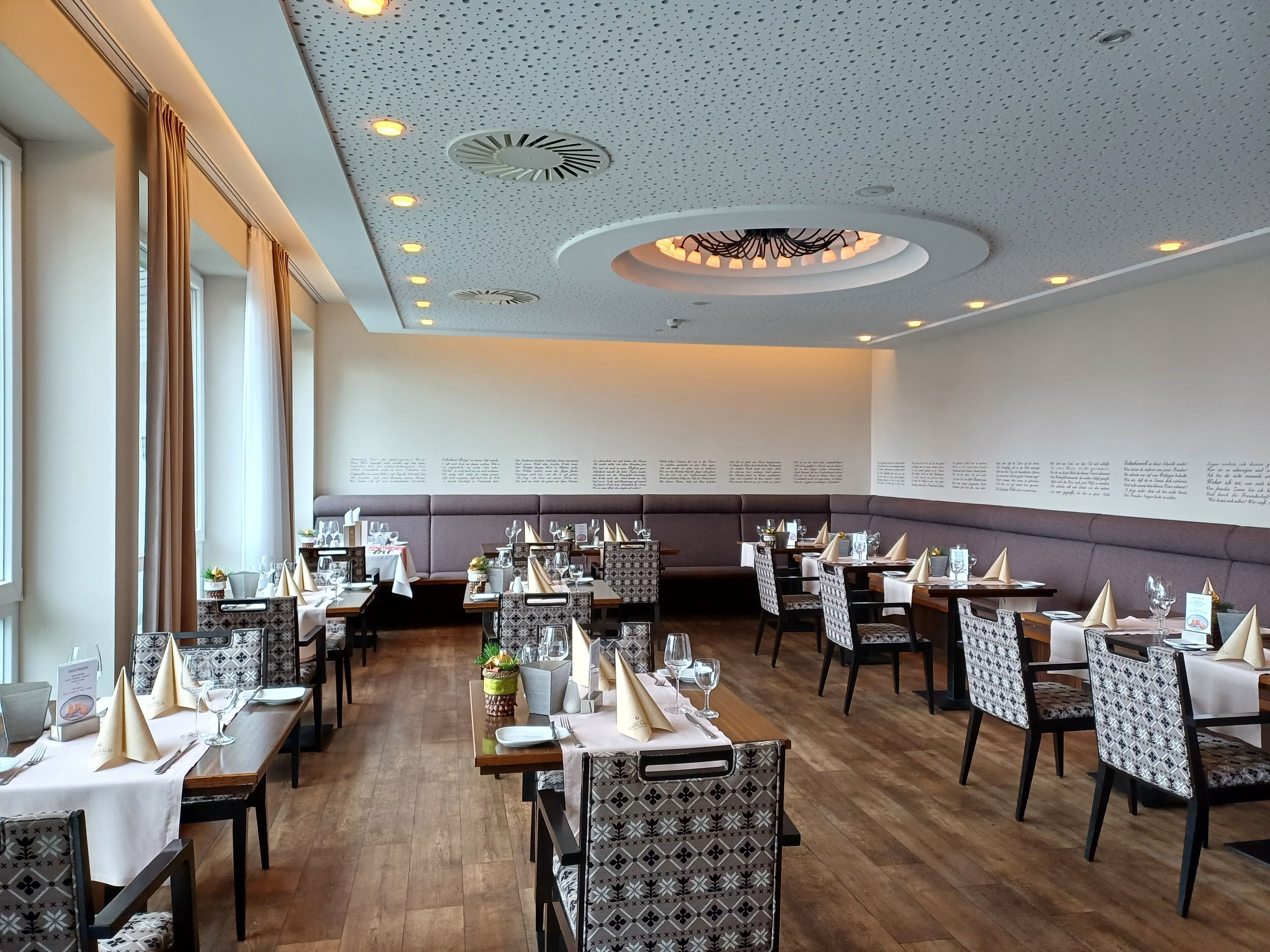 A restaurant with multiple tables, chairs, and a high ceiling with decorative lighting.