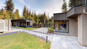 Una casa moderna con un patio, una pequeña terraza y un amplio ventanal con vistas a un área boscosa.