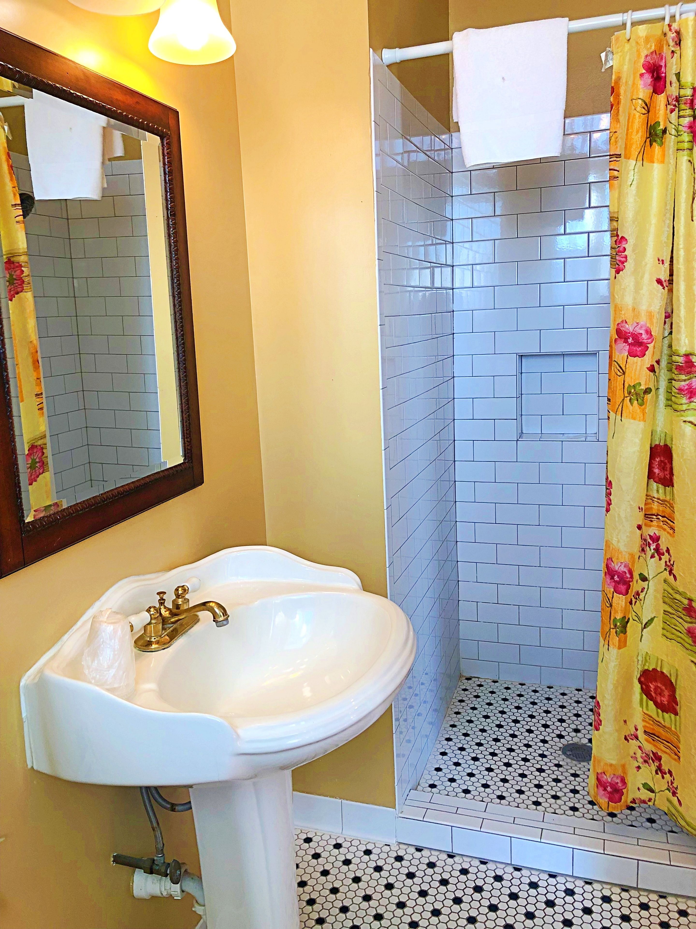 Un baño con un lavabo blanco, una ducha con cortina estampada y suelo de baldosas.
