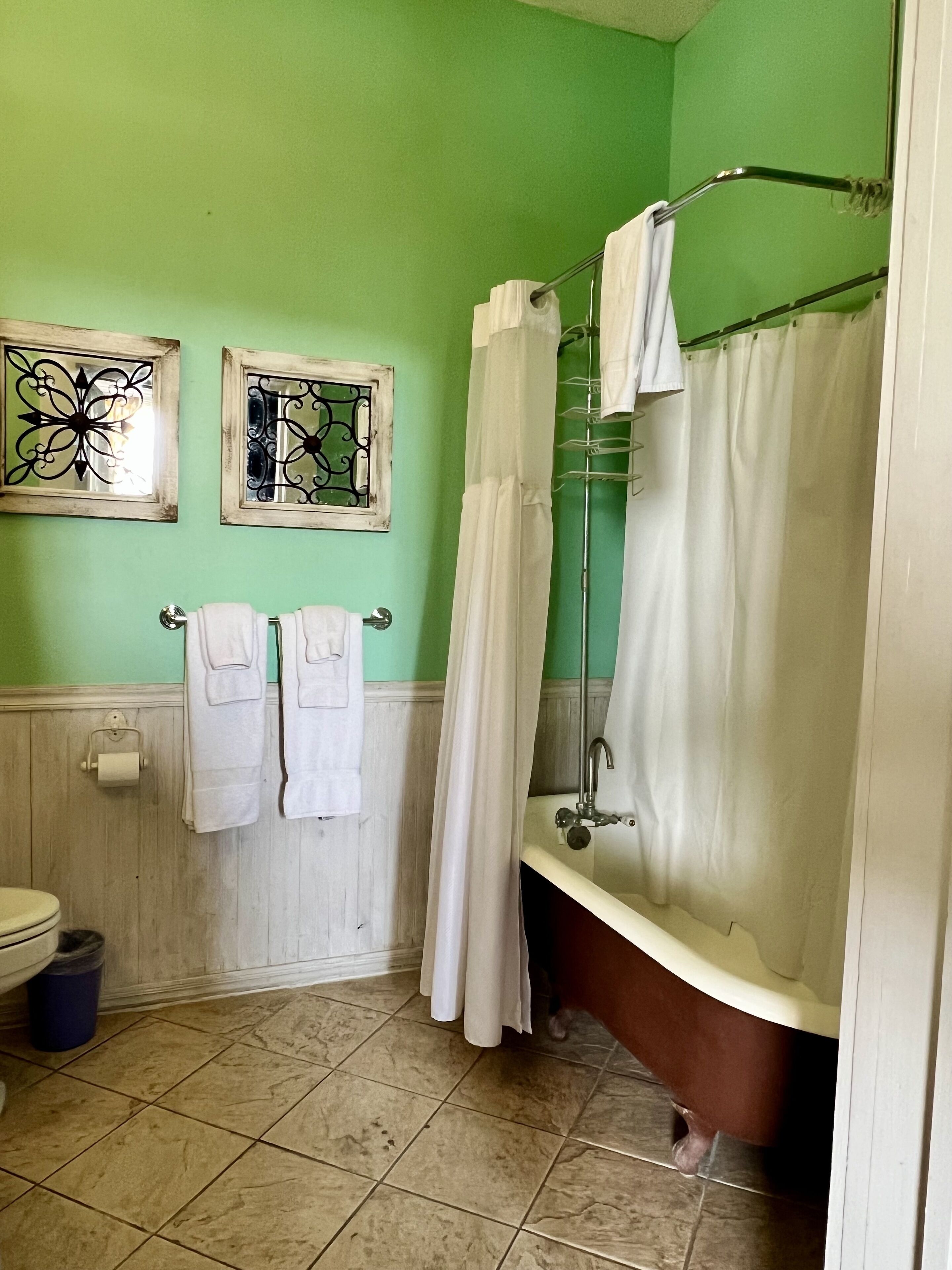 Casa de banho com parede verde, dois espelhos decorativos emoldurados, uma banheira branca e uma cortina de chuveiro.