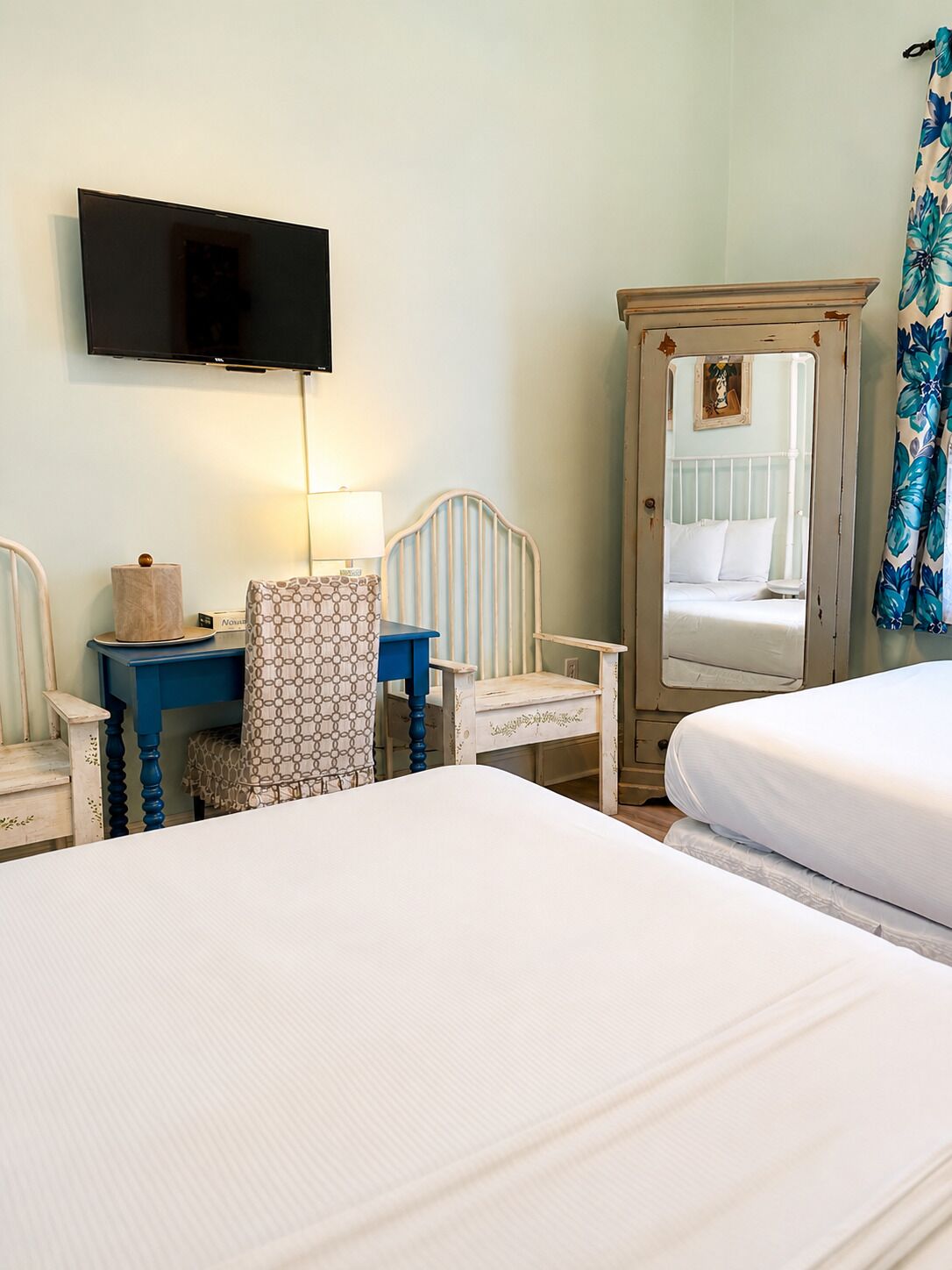 A hotel room with two beds, a desk with a lamp, a television, and a mirror.