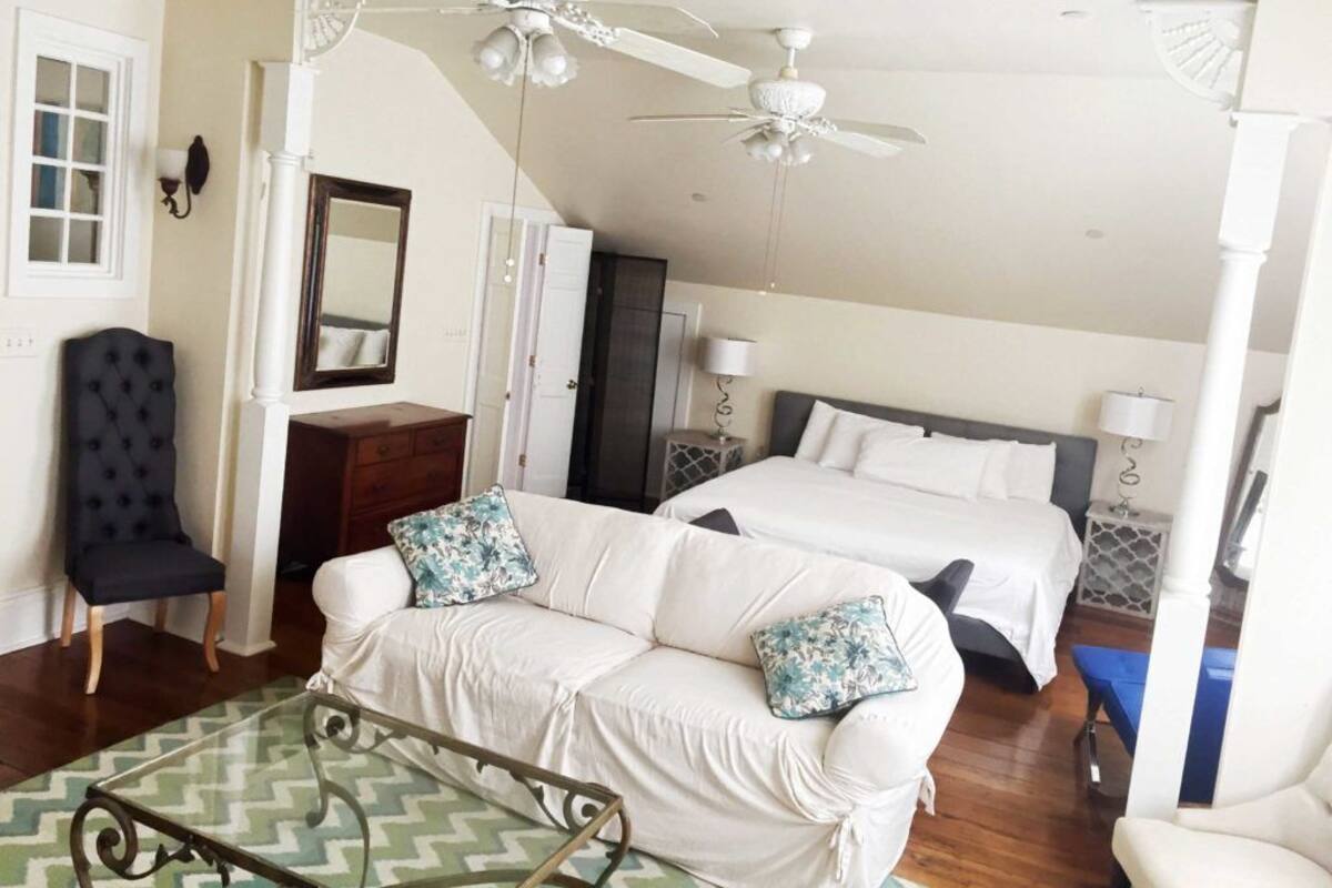 A hotel room with a white sofa, two beds, a ceiling fan, and a mirror.