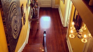 A wooden staircase with a chandelier, a door with a window, and a wall with framed pictures. - Creole Gardens Guesthouse and Inn (New Orleans)