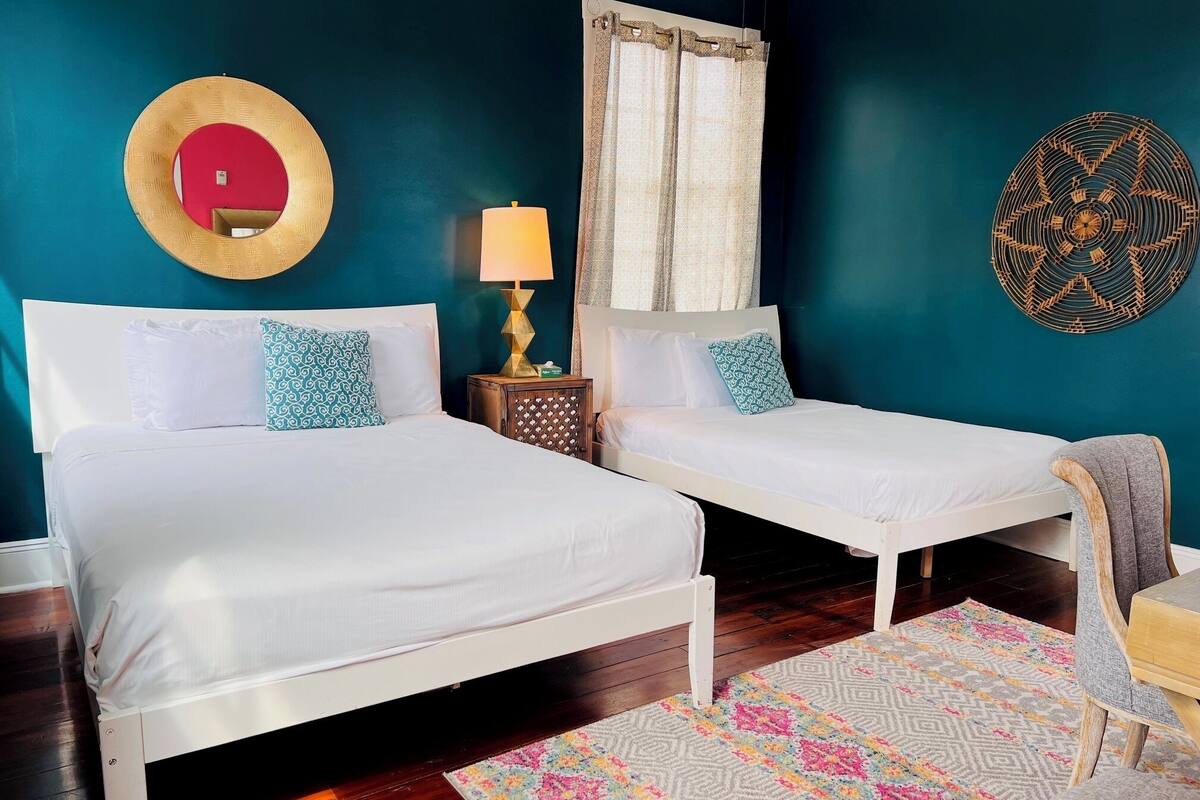 A room with two beds, a nightstand with a lamp, a wall mirror, and a patterned rug.