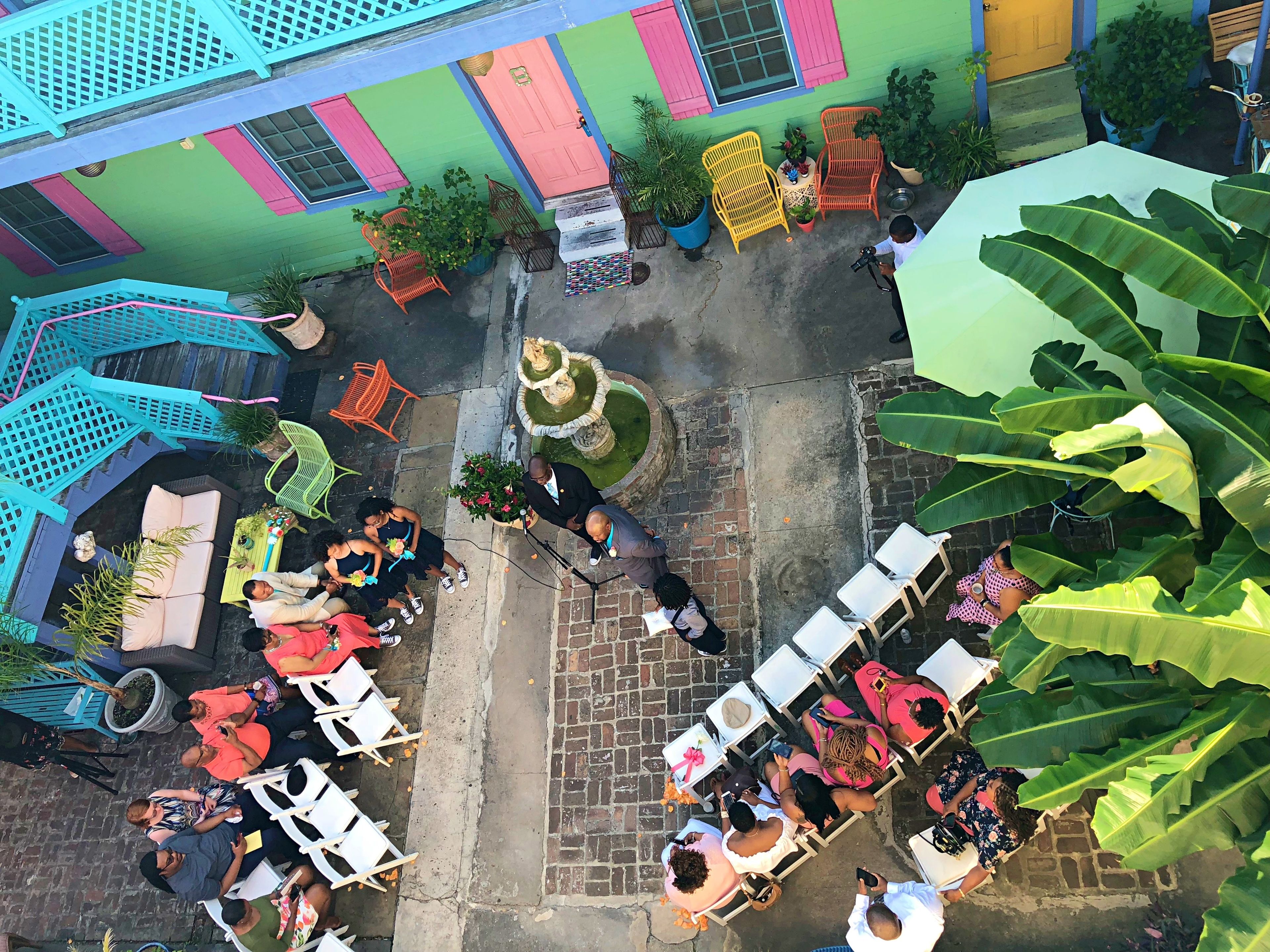 Un espace extérieur aménagé avec des tables et des chaises, entouré de bâtiments aux couleurs vives et de plantes en pot.
