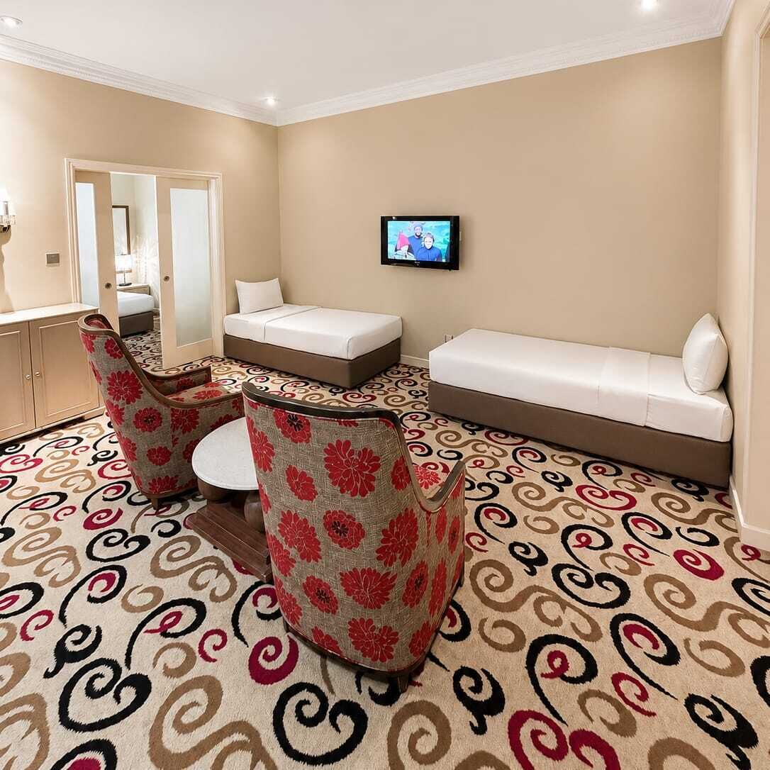 A hotel room with a bed, a sofa, two chairs, a TV, and a mirror.