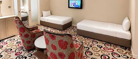 A hotel room with a bed, a sofa, two chairs, a TV, and a mirror.