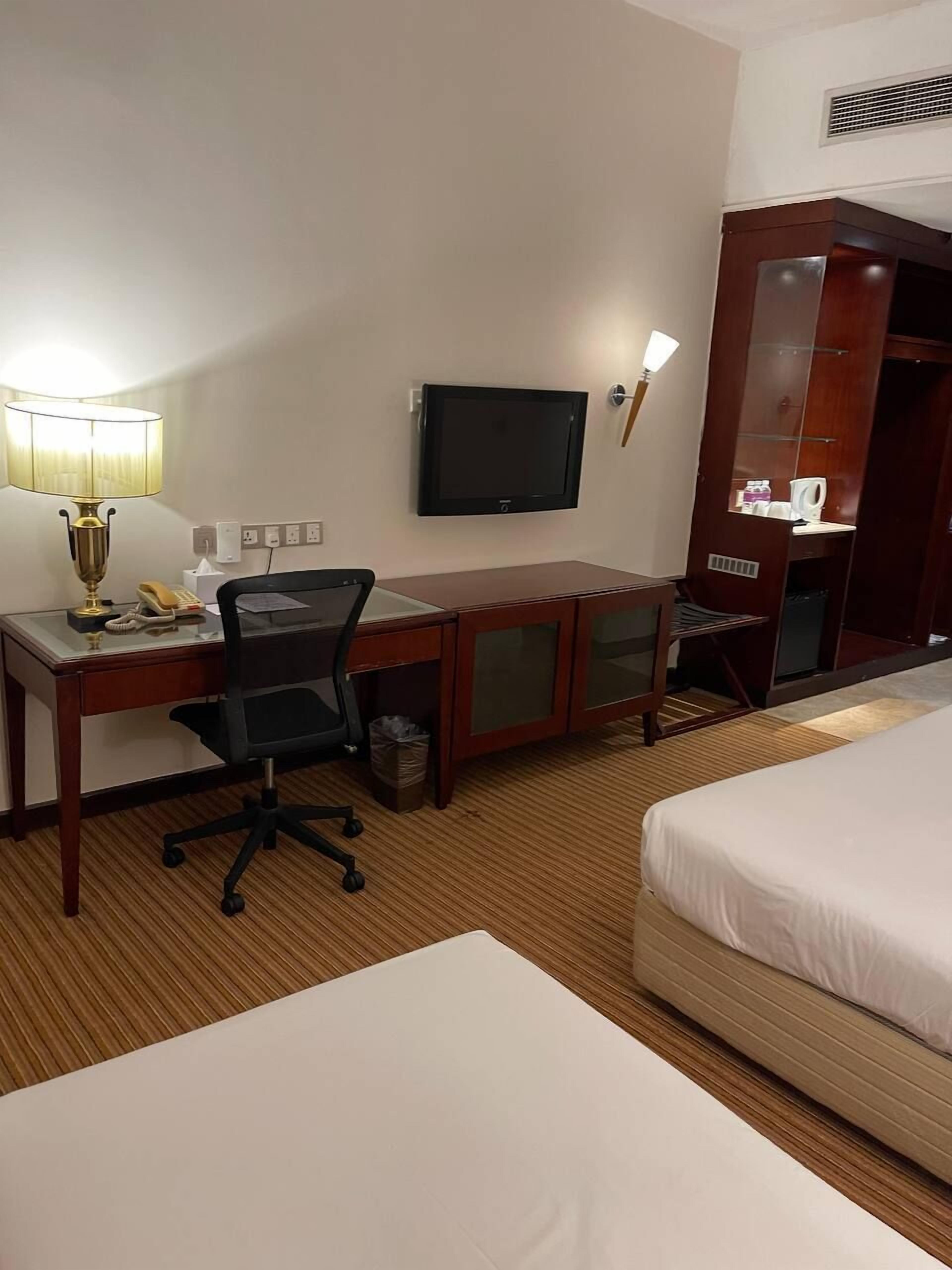 A hotel room with a desk, chair, TV, and two beds.