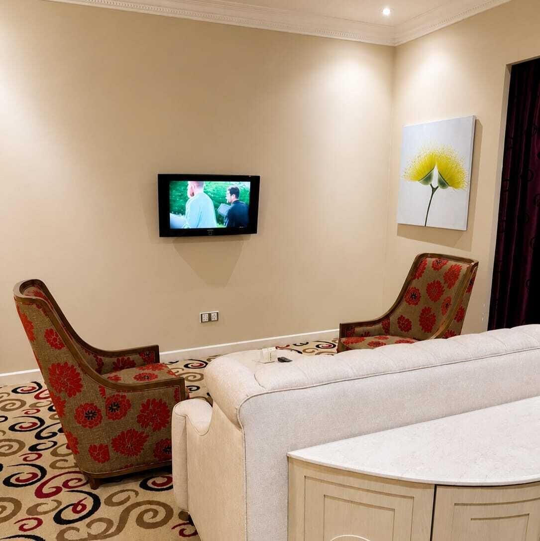 Habitación de hotel con televisión, dos sillones estampados, sofá y alfombra con diseño.