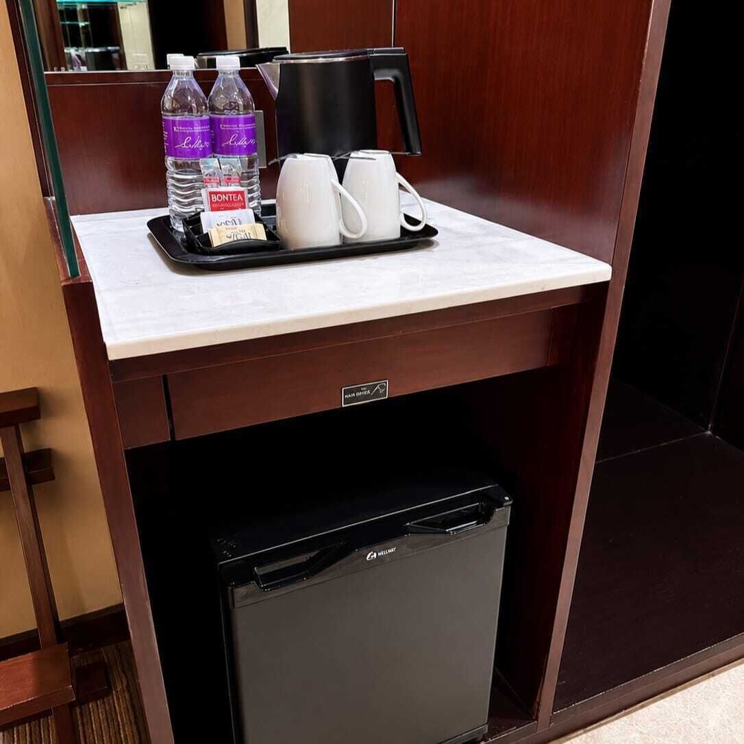 A compact hotel room with a small kitchenette, a mini fridge, a coffee maker, and a tray with bottled water and cups.
