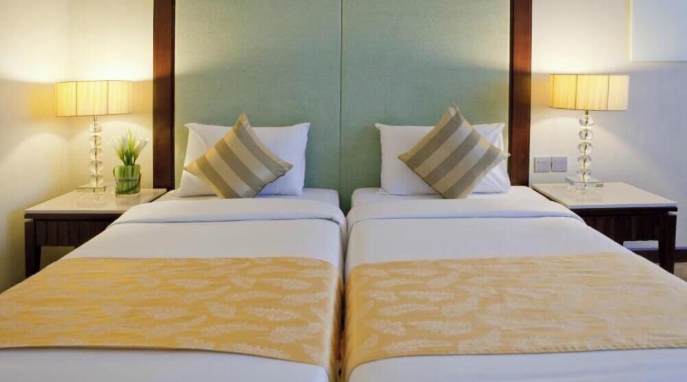 Quarto de hotel com duas camas, cada uma com travesseiro e luminária na mesinha de cabeceira.