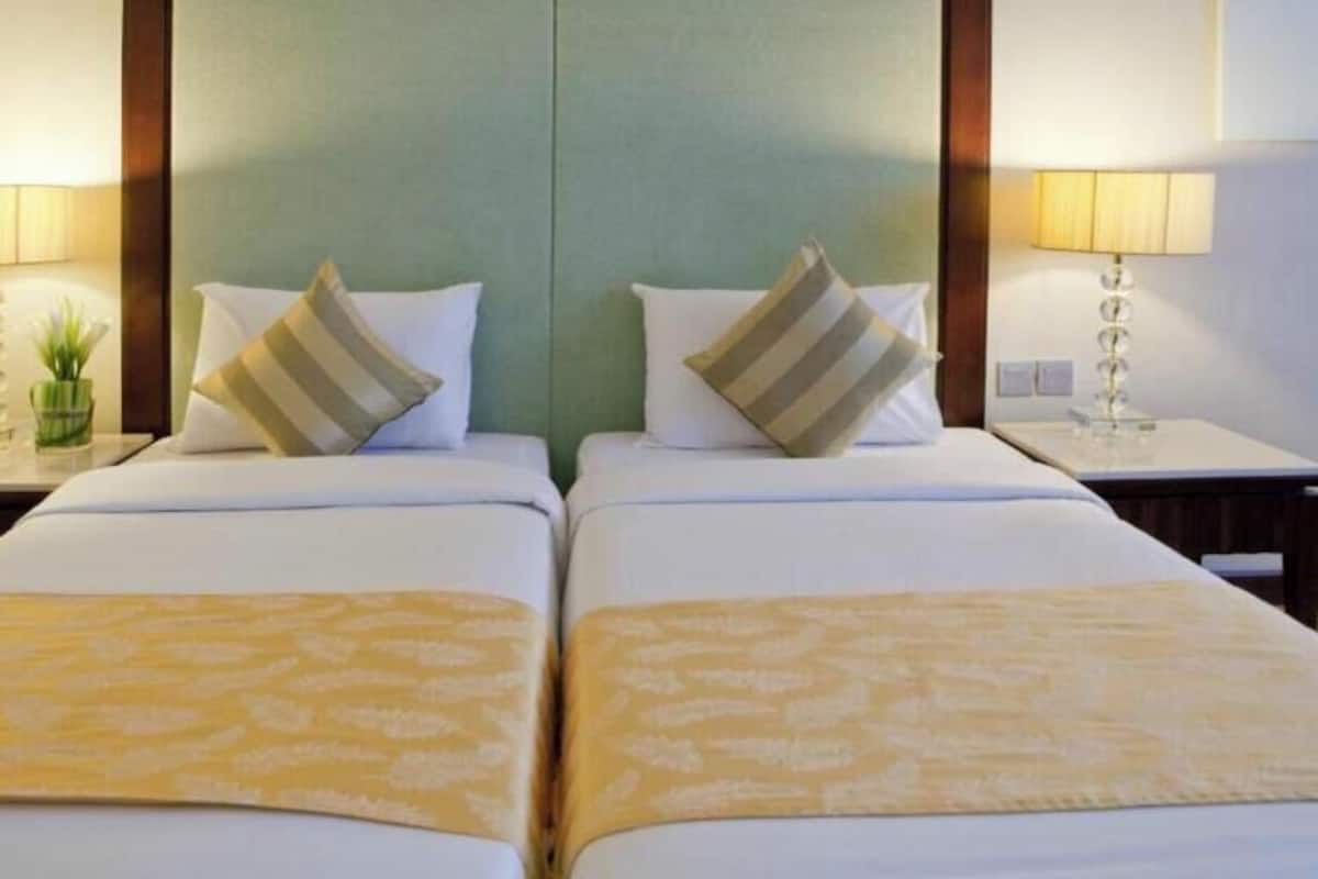 Quarto de hotel com duas camas, cada uma com travesseiro e luminária na mesinha de cabeceira.