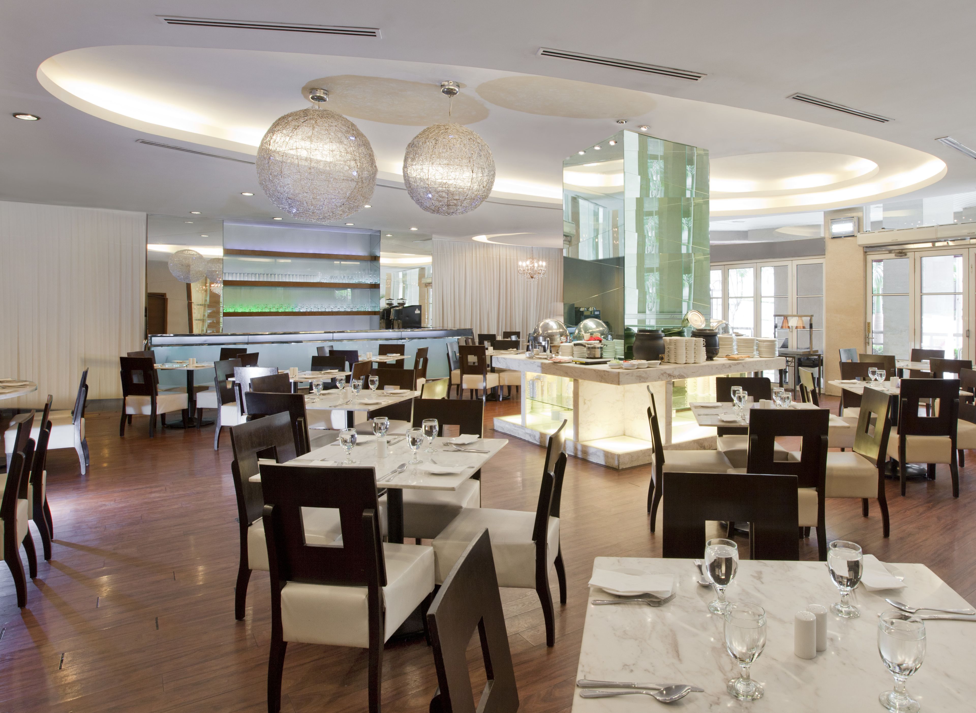 A spacious dining area with multiple tables and chairs, a central bar, and a modern chandelier.