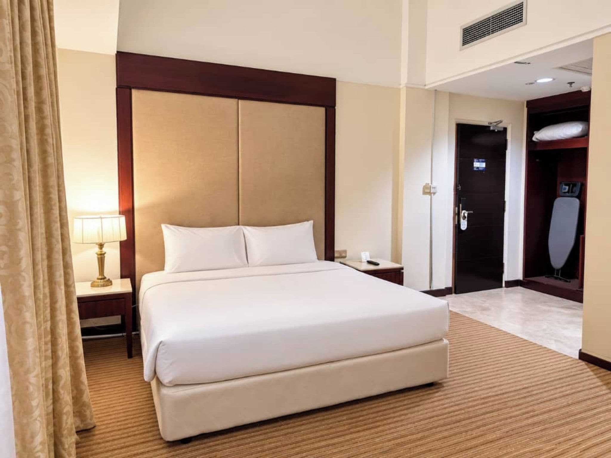 Een hotelkamer met een groot bed, een nachtkastje, een lamp en een deur naar een badkamer.