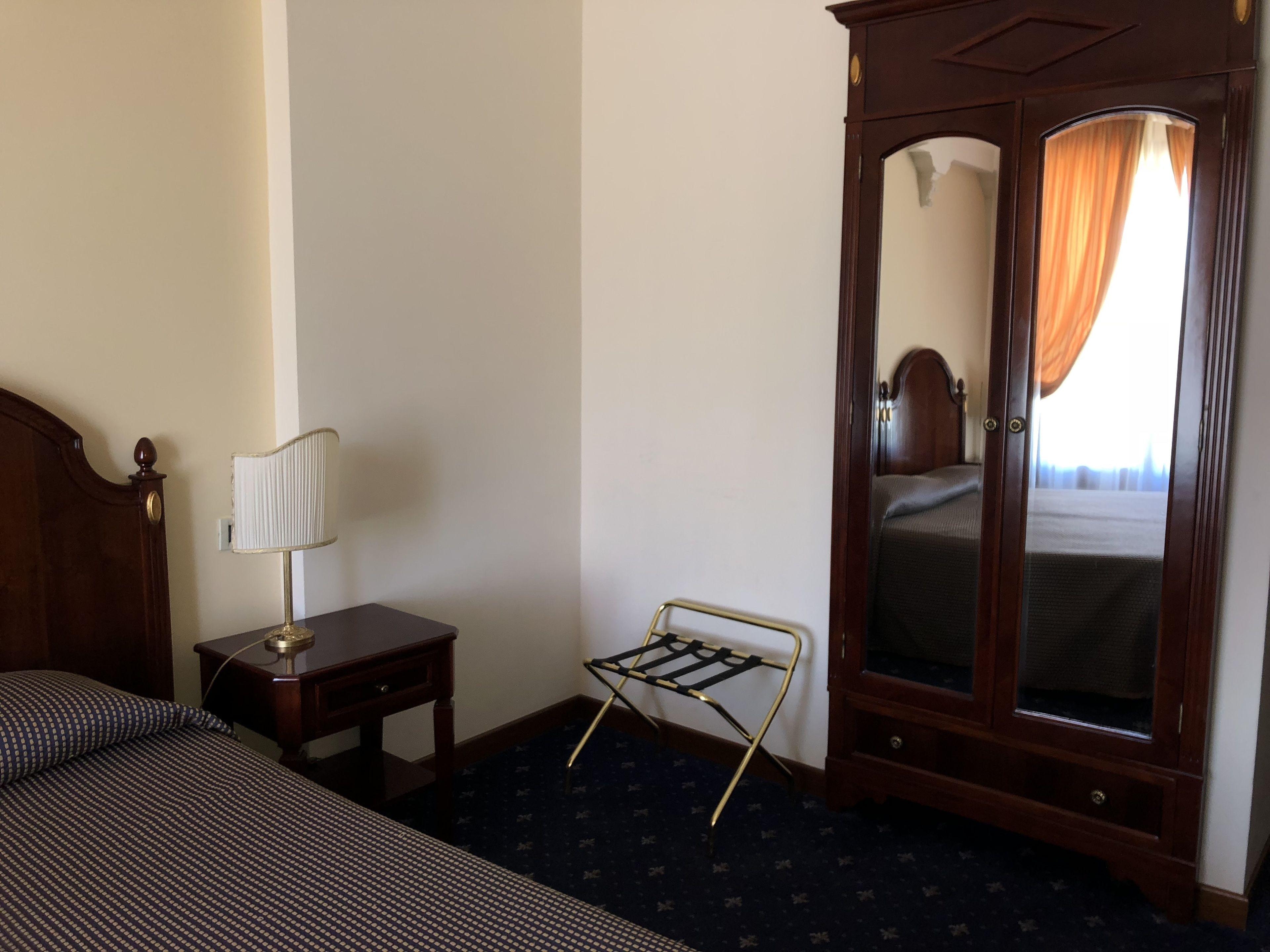 Una habitación de hotel con cama, mesita de noche, lámpara, espejo y armario.