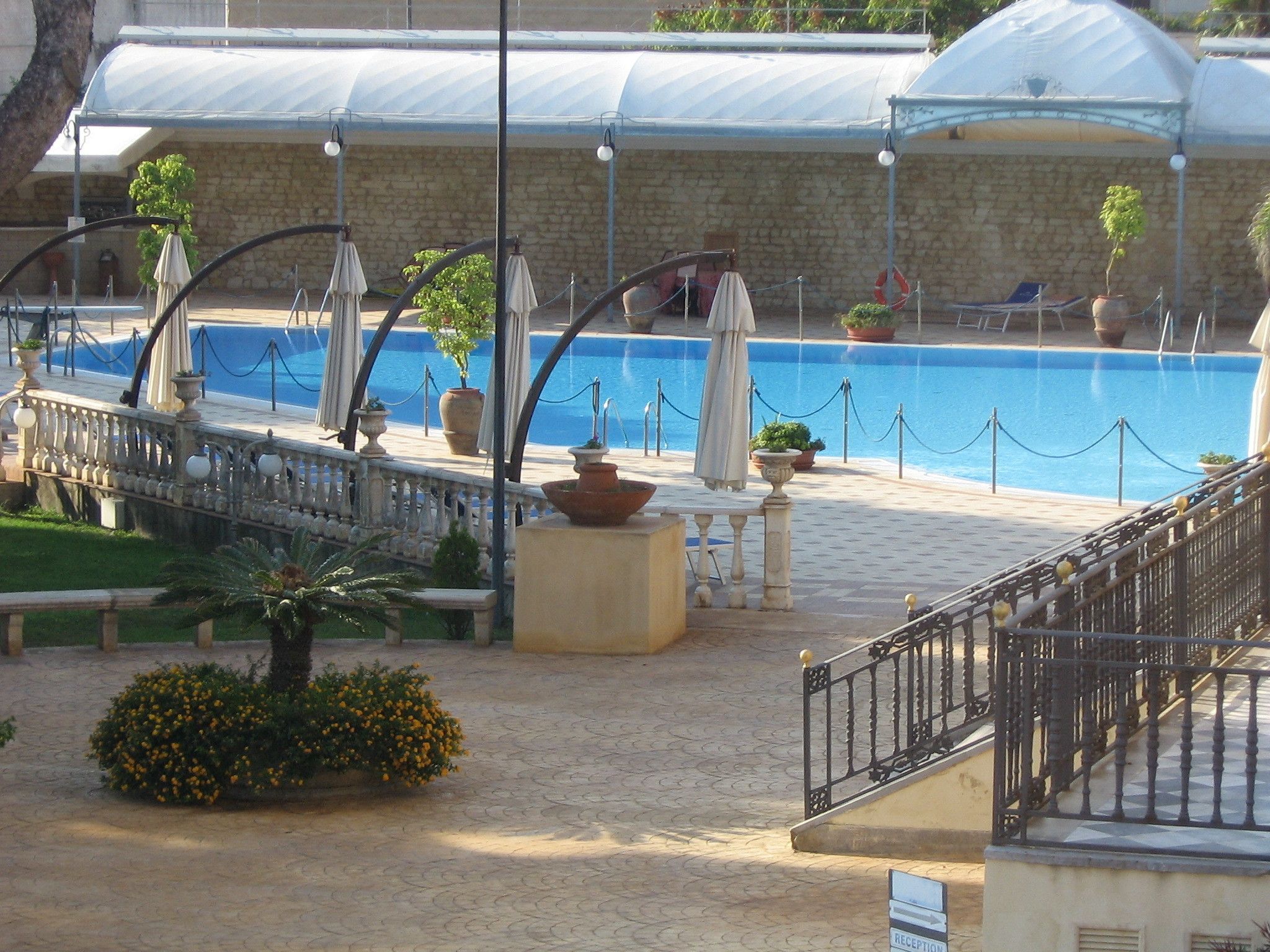 Ein Poolbereich mit einer Steinmauer, Sonnenschirmen und Topfpflanzen.