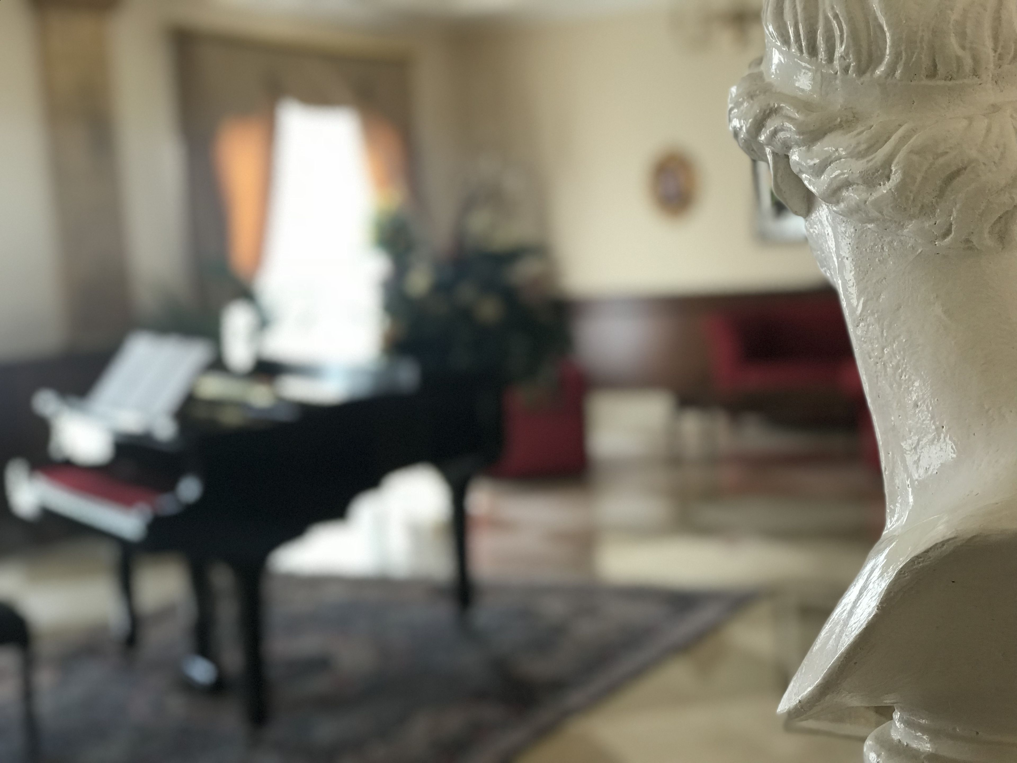 A statue in a room with a piano and a red sofa.