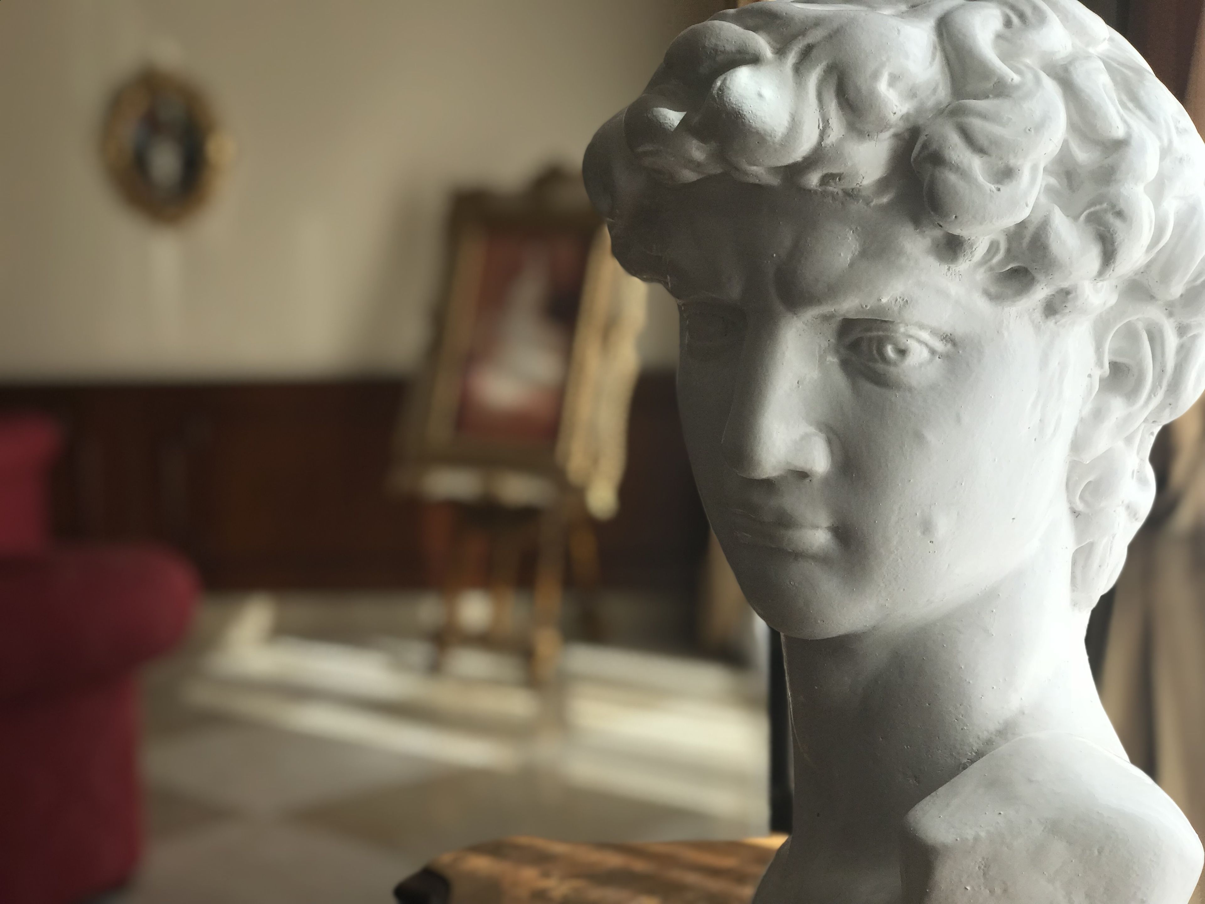 Um busto em escultura em um aposento com piso de madeira e um quadro emoldurado na parede.