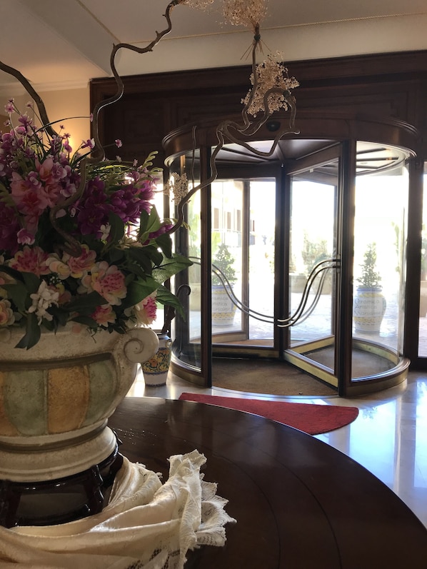 Un vestíbulo con un gran arreglo floral, una puerta de cristal de entrada y un candelabro.
