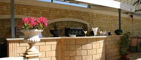 An outdoor bar area with a stone wall, a potted plant, and a grill.