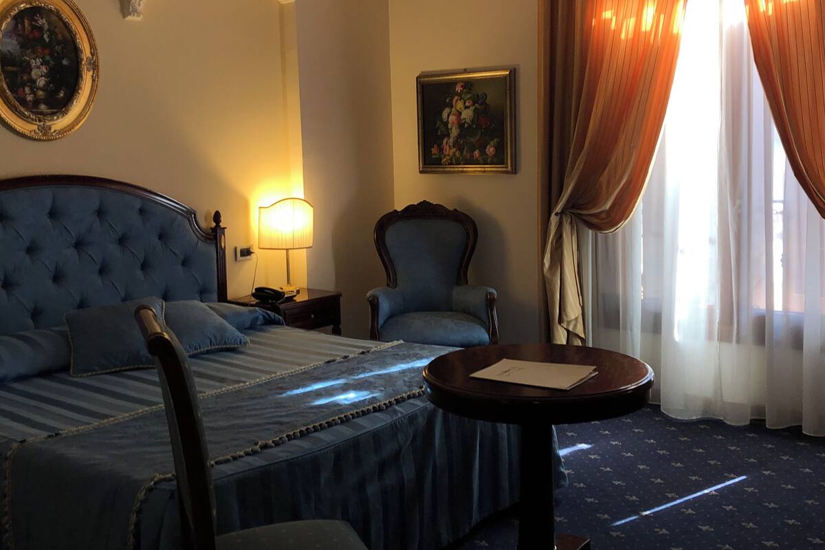 A hotel room with a large bed, two armchairs, a small table, a lamp, and a painting on the wall.
