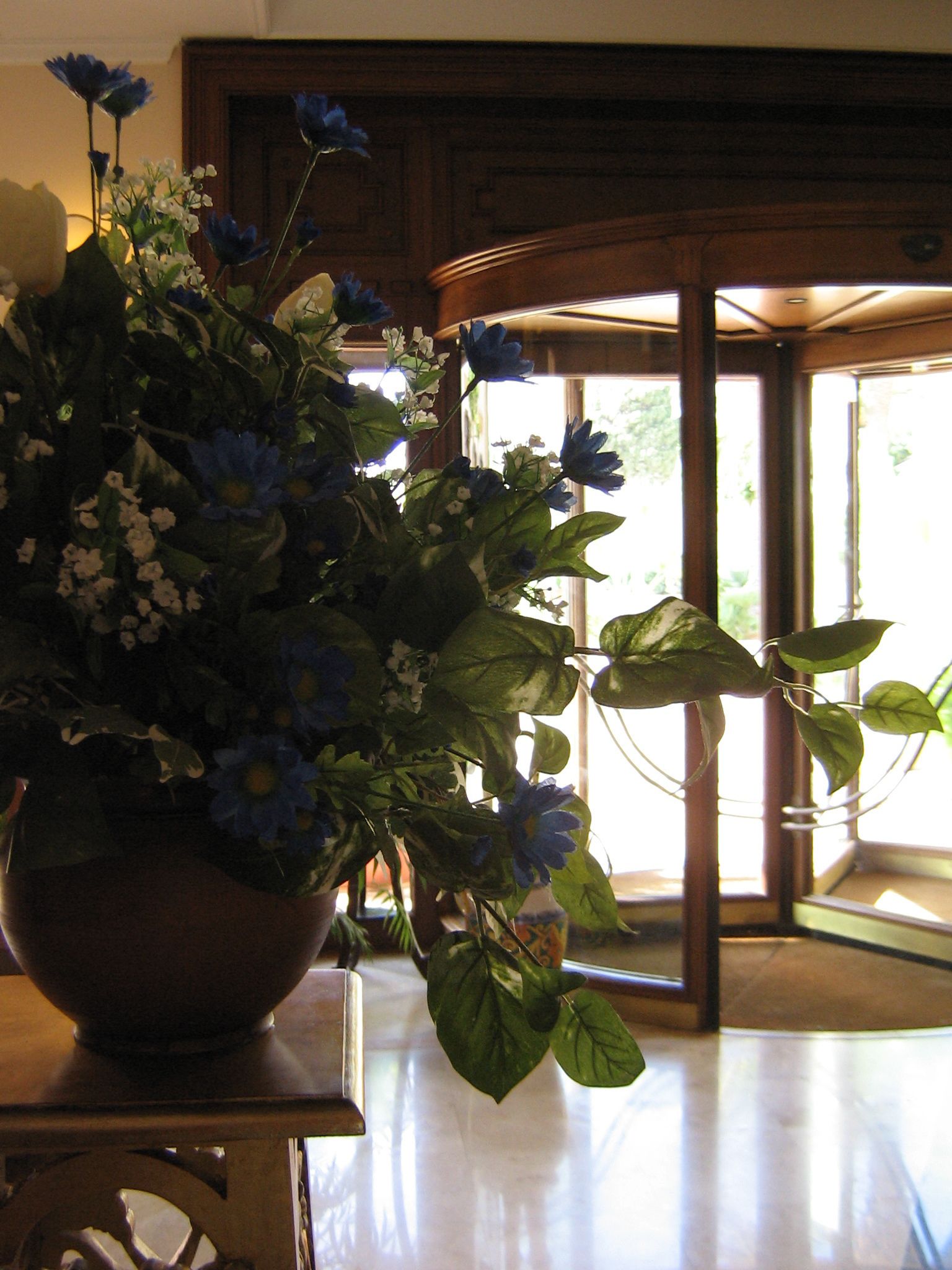 Una planta en maceta con flores azules sobre una mesa de madera en una habitación con un ventanal y una puerta.