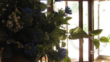 Una planta en maceta con flores azules sobre una mesa de madera en una habitación con un ventanal y una puerta.