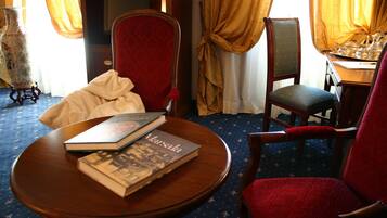 A room with a round wooden table, two red upholstered chairs, a bookshelf, and a large vase.