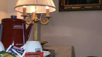 A table with a red coffee maker, a white coffee pot, a lamp, and some food items.