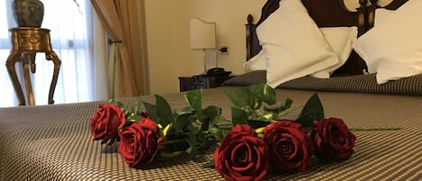 Una habitación de hotel con una cama, una mesita de noche, una lámpara y un jarrón con flores.