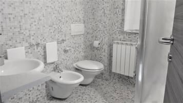 Et badeværelse med toilet, bidet og vask, flisegulv og et håndklædetørrestativ.