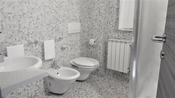 A bathroom with a toilet, bidet, and sink, tiled floor, and a towel rack.