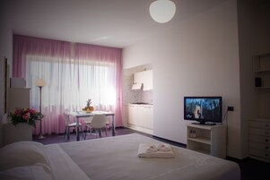 Una habitación de hotel con cama, escritorio, televisión y kitchenette.