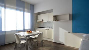 A modern kitchen with white cabinets, a dining table with chairs, and a fruit bowl.