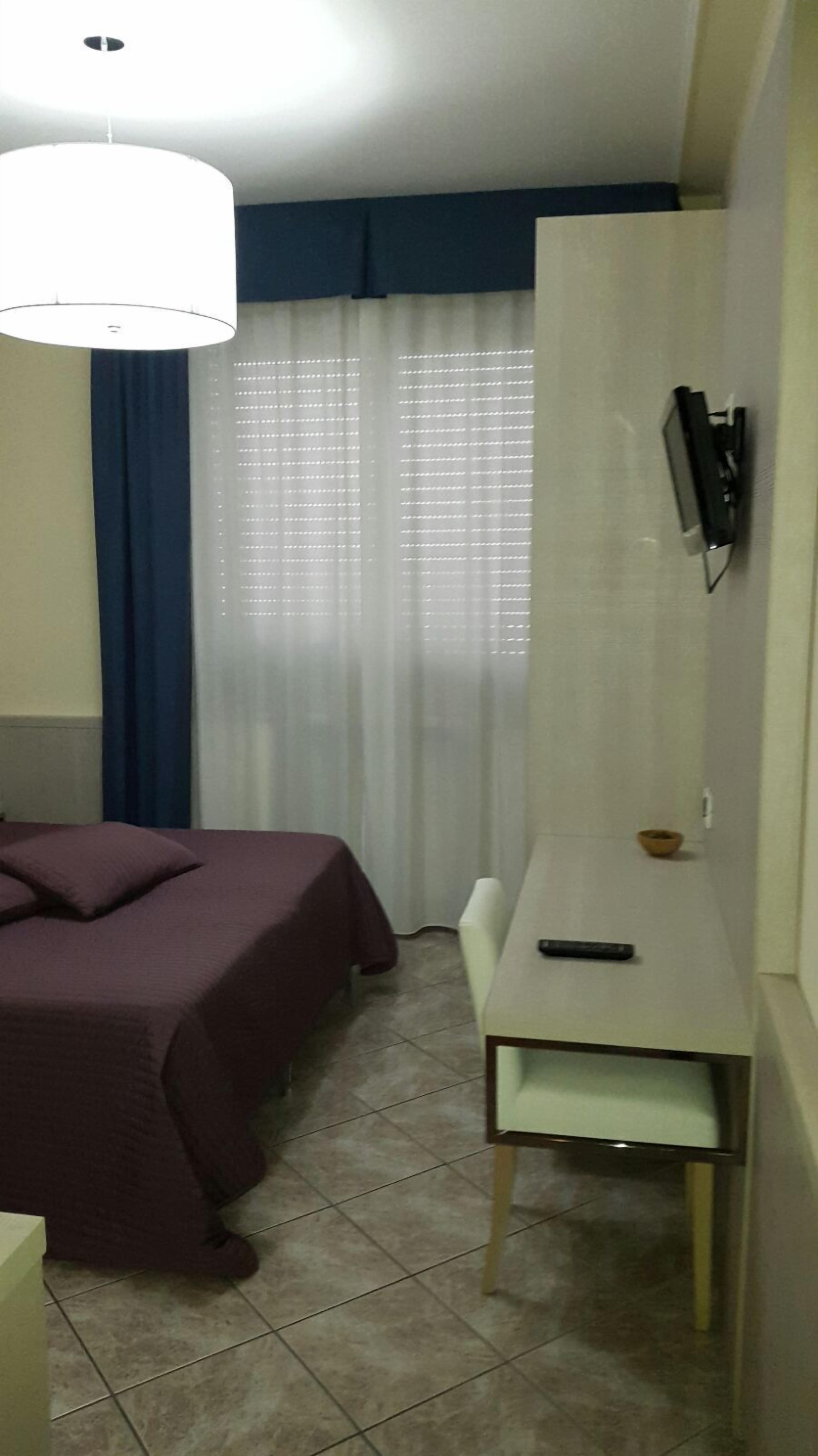 Ein Hotelzimmer mit Bett, Schreibtisch, Stuhl, Wandfernseher und einem Fenster mit Vorhängen.