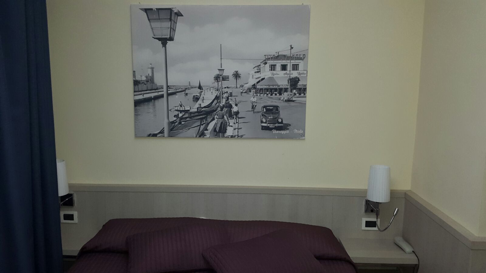 Une chambre d’hôtel avec un lit, une table de chevet avec une lampe et un tableau accroché au mur représentant un paysage de bord de mer.