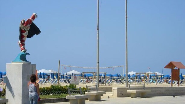 A beachside promenade with a statue, sun loungers, and umbrellas. - Hotel Bella Riviera (Viareggio)