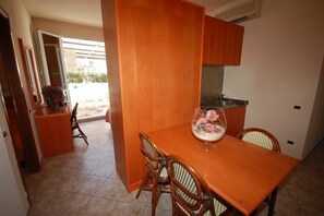 A compact kitchen with wooden cabinets, a dining table, and chairs. - Hotel Bella Riviera (Viareggio)