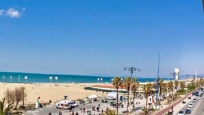 A beachside view with a clear sky, a sandy beach, palm trees, and a road with vehicles. - Hotel Bella Riviera (Viareggio)